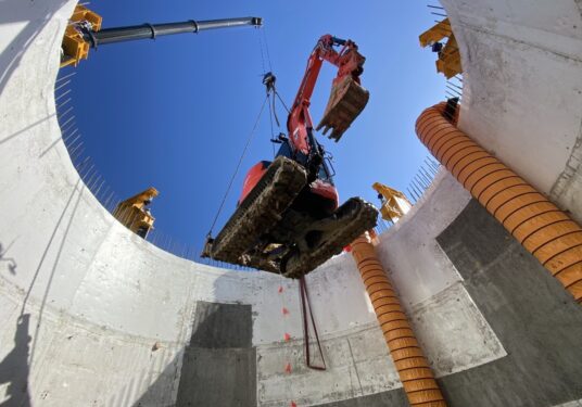 Excavator being lowered into a deep concrete shaft on a Queensland construction site.